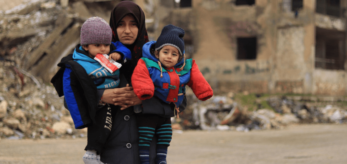 سيدة تحمل طفليْها في مدينة حلب التي تعرّضت للدمار في سوريا