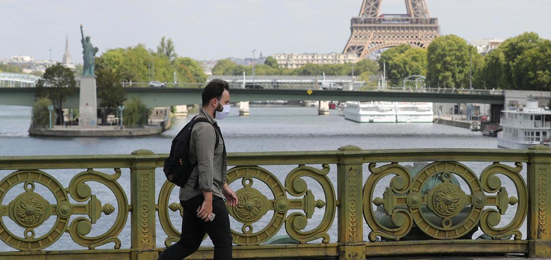 رجل يعبر جسر ميرابو قرب برج ايفل ونسخة تمثال الحرية في باريس