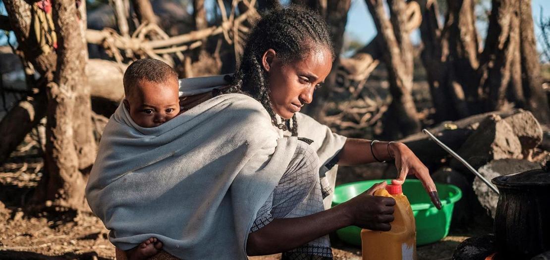 امرأة تحمل ابنها وتطبخ في قرية بيسوبر في إقليم تغيراي في شمال إثيوبيا، 9 كانون الأول 2020