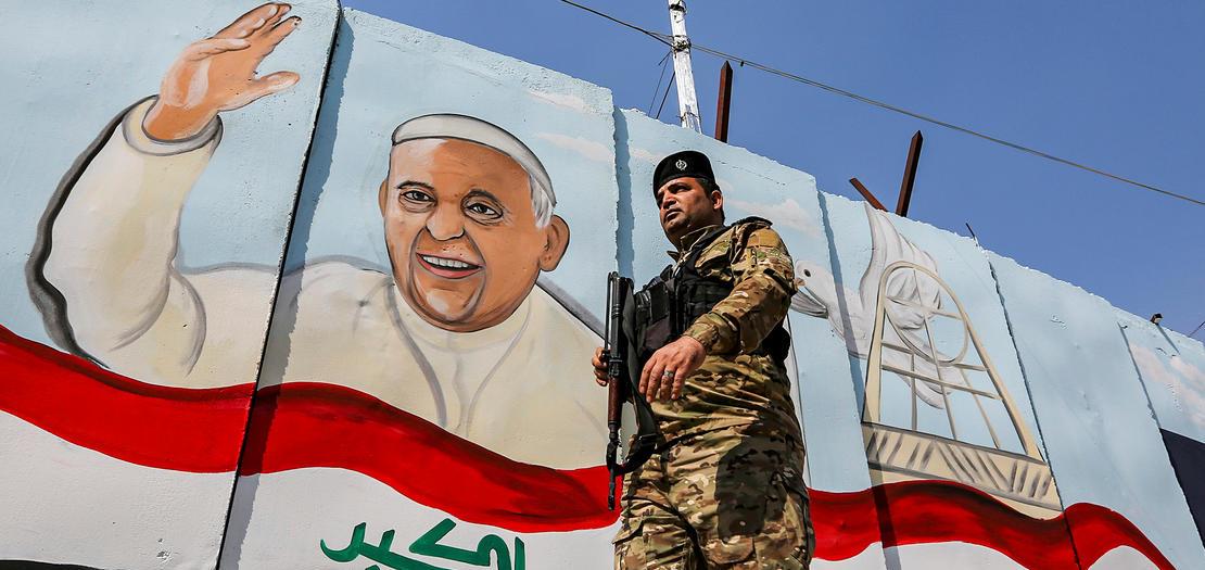 عنصر من القوات العراقية يمر أمام جدارية عليها صورة للبابا قرب كنيسة سيدة النجاة في حي الكرادة ببغداد، 1 آذار 2021