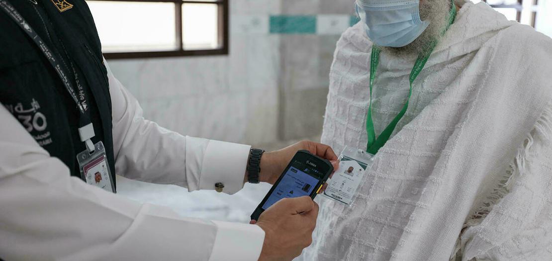 موظف سعودي (يسار) يستخدم ماسحا ضوئيا لقراءة البطاقة الذكية لحاج دون تلامس بشري في مكة في 18 تموز 2021