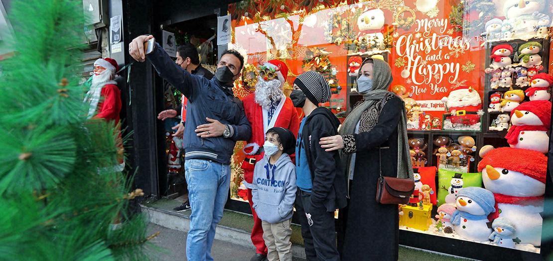 أفراد عائلة إيرانية يلتقطون صورة "سيلفي" مع رجل يرتدي زي "بابا نويل" خارج متجر يبيع زينة عيد الميلاد في طهران، في 24 كانون الأول 2021.