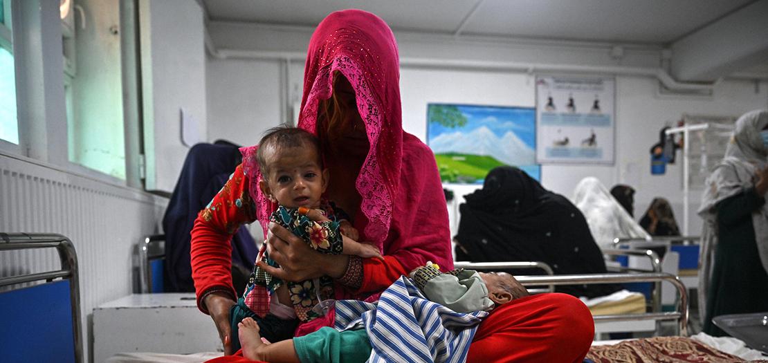 صورة ملتقطة في 21 تموز 2022 تظهر بريشنا على فراش مع طفليها التوأمين في قسم سوء التغذية في مستشفى بوست الذي تديره منظمة "أطباء بلا حدود" في محافظة هلمند في جنوب أفغانستان