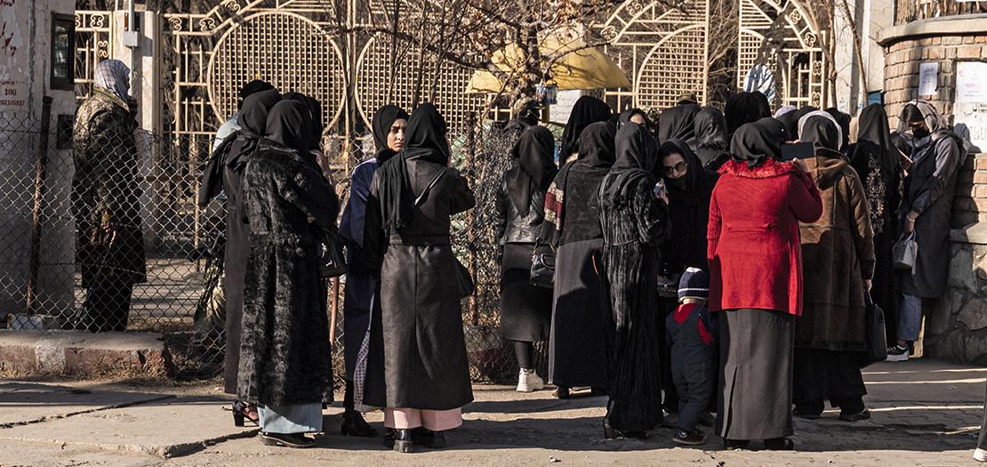 طالبات جامعات أفغانيات يقفن أمام أفراد أمن طالبان قرب إحدى الجامعات في كابول في 21 كانون الأول 2022