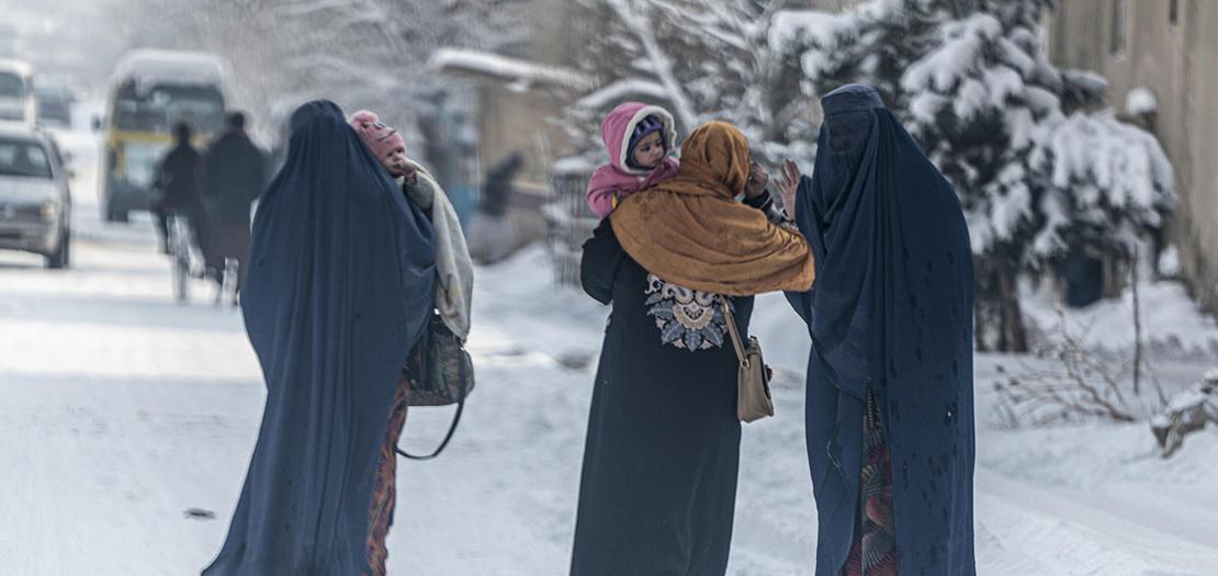 أفغانيات يحملن أطفالا يمشين في شارع مكسو بالثلج في كابول في 23 كانون الثاني 2023