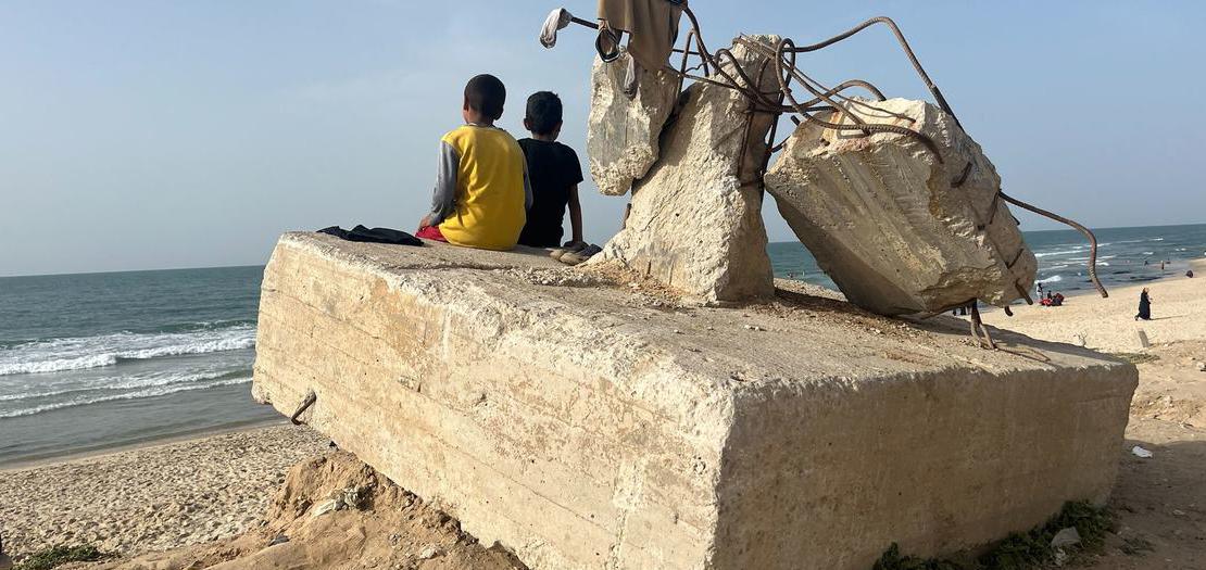 طفلان فلسطينيان يجلسان على كتلة خرسانية على الشاطئ بمدينة رفح، جنوب غزة